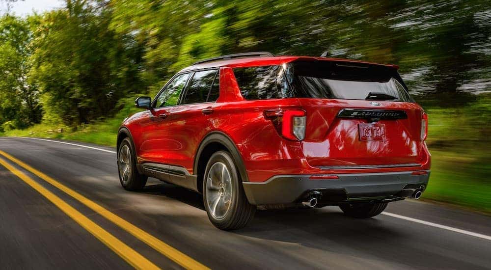 A red 2022 Ford Explorer for sale is driving on a tree-lined road.