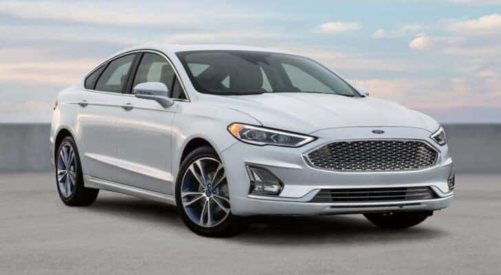 A white 2020 Ford Fusion is shown parked at a used car dealer near Owosso.