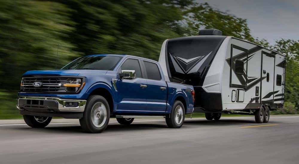 A blue 2025 Ford F-150 is towing a trailer on a highway.