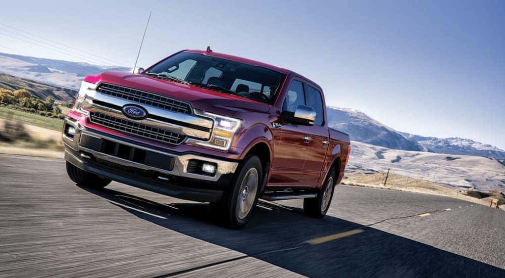 A red 2020 Ford F-150 driving on a highway to a used truck dealer near Lansing.