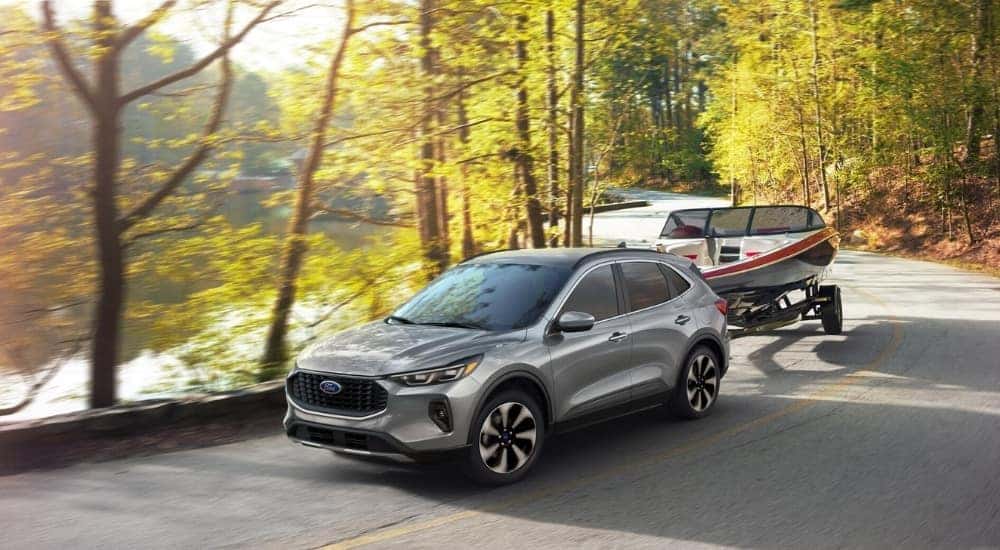 A silver 2025 Ford Escape Platinum towing a boat past a small lake.