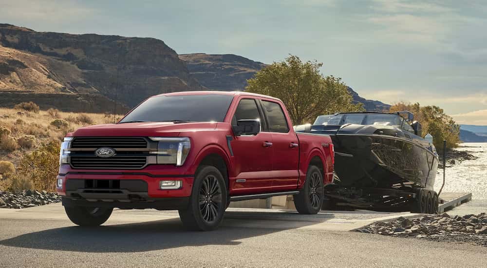 A red 2025 Ford F-150 for sale near Lansing towing a boat at a lake.