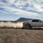 Side view of a grey 2025 Ford F-150 Raptor kicking up a trail of dust while off-roading.
