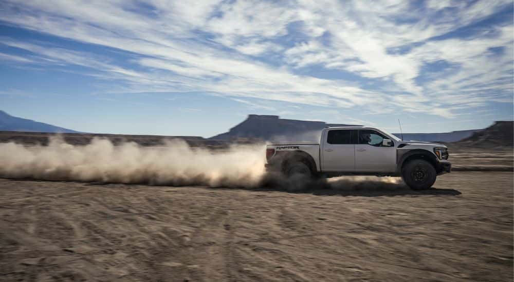 Side view of a grey 2025 Ford F-150 Raptor kicking up a trail of dust while off-roading.