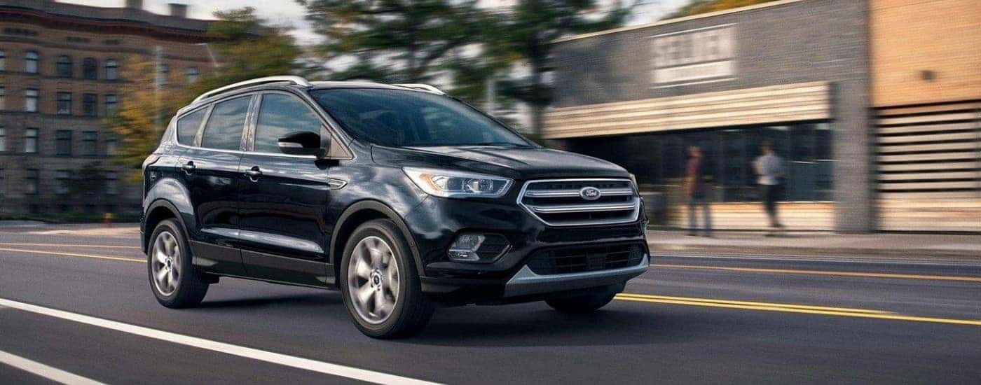 A black 2019 Ford Escape is driving through a town center.
