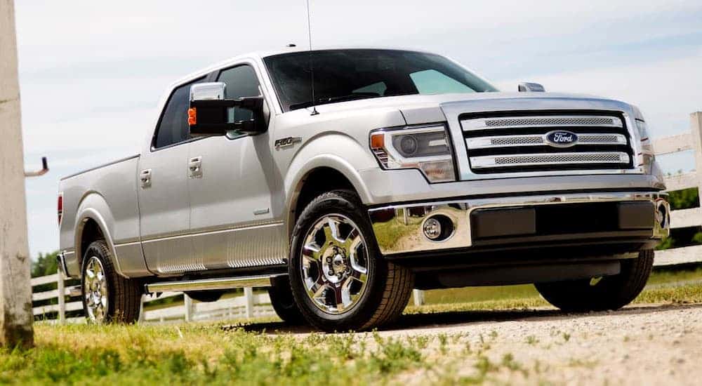 White used 2014 Ford F-150 Lariat for sale driving by a fence.