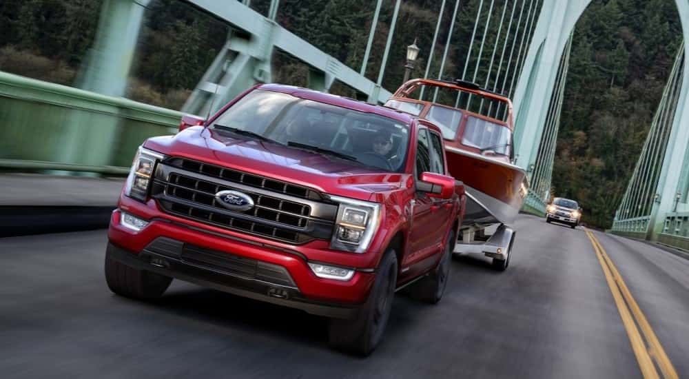 Red 2021 Ford F-150 towing a boat across a bridge.