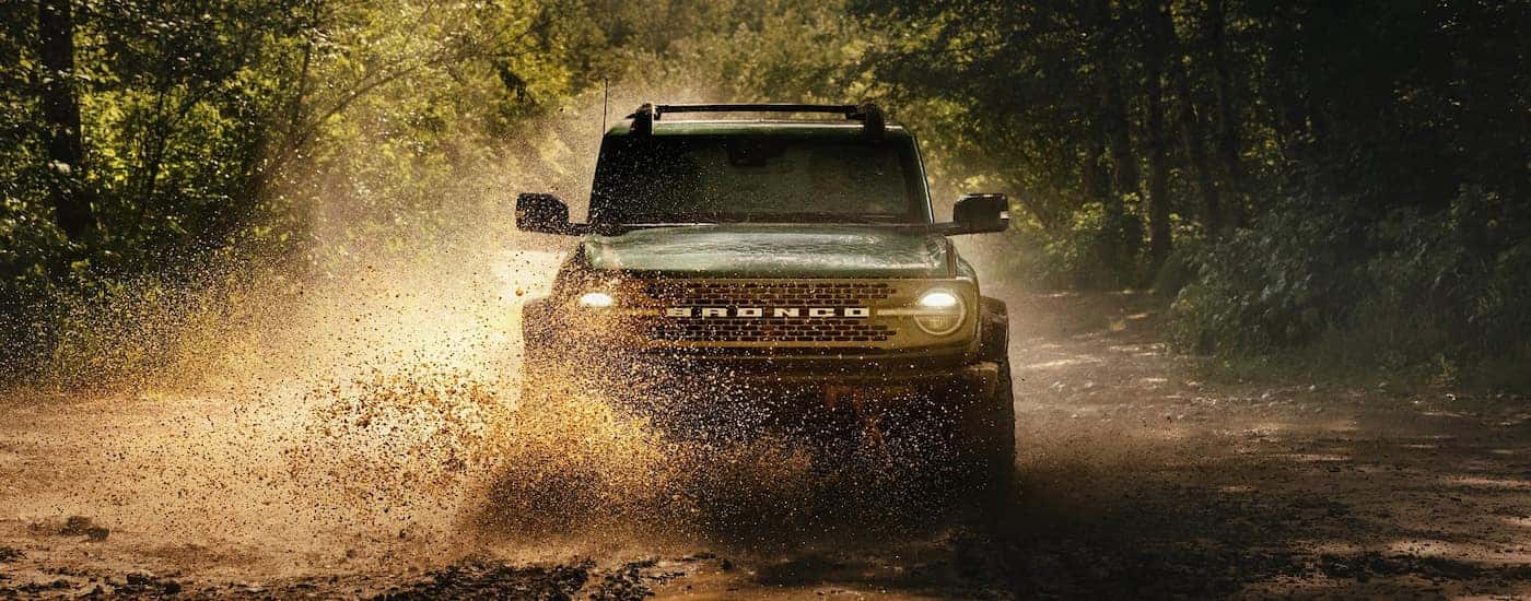 Dark green 2025 Ford Bronco driving over a mud puddle.