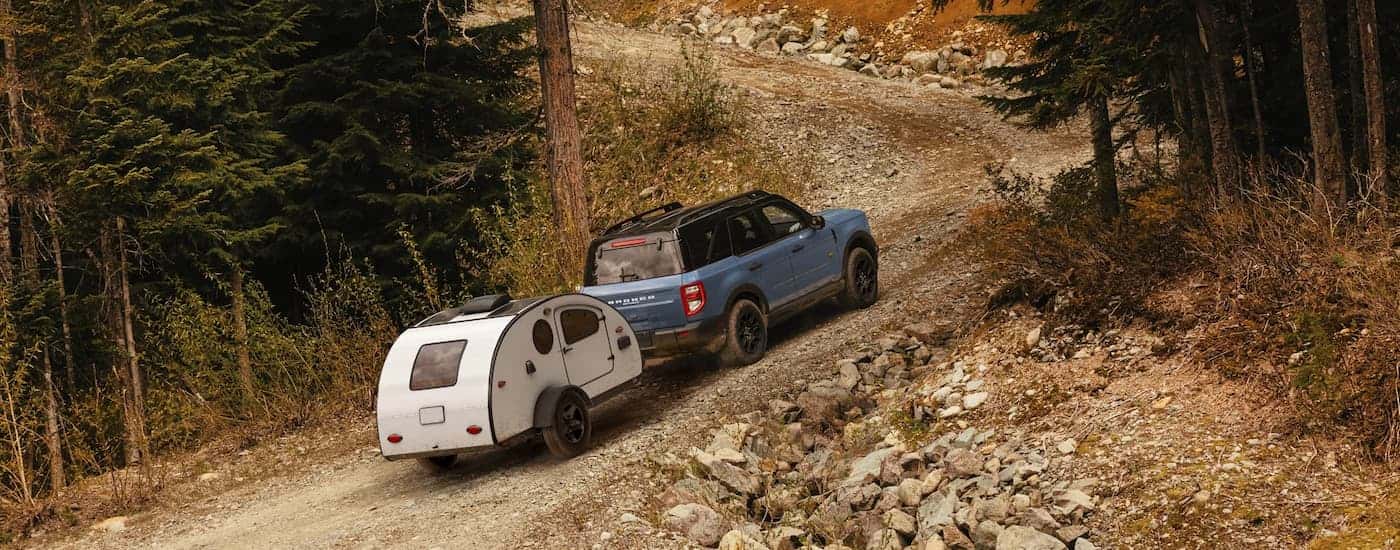 A blue 2025 Ford Bronco Sport off-roading on a dirt trail towing a camper