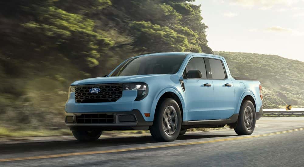 Blue 2026 Ford Maverick driving on a winding road near a lake