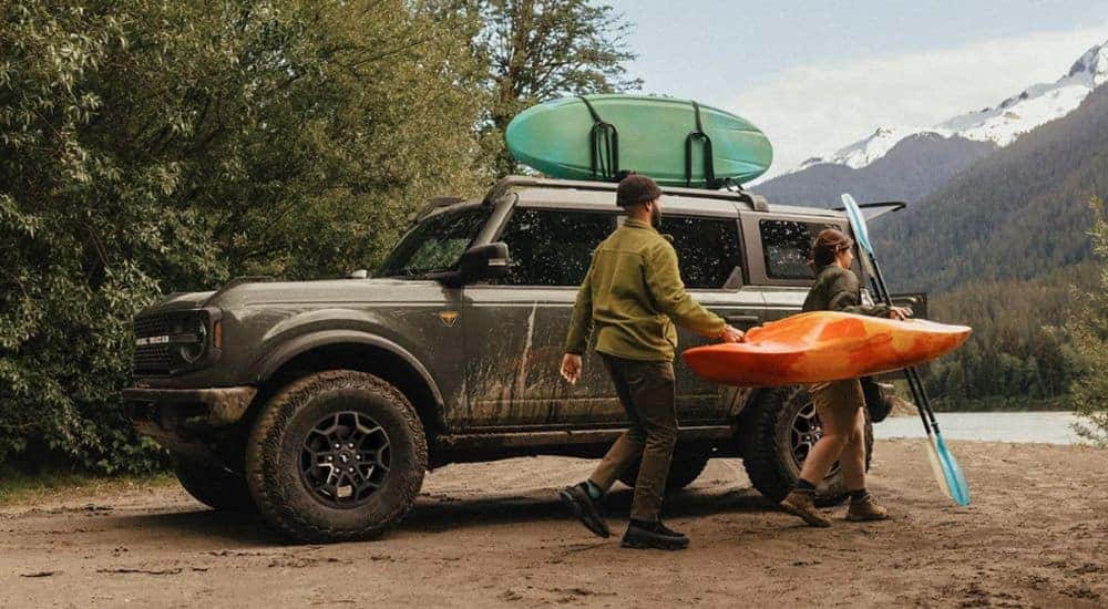 Two people carrying a kayak next to a dark green 2026 Ford Bronco.