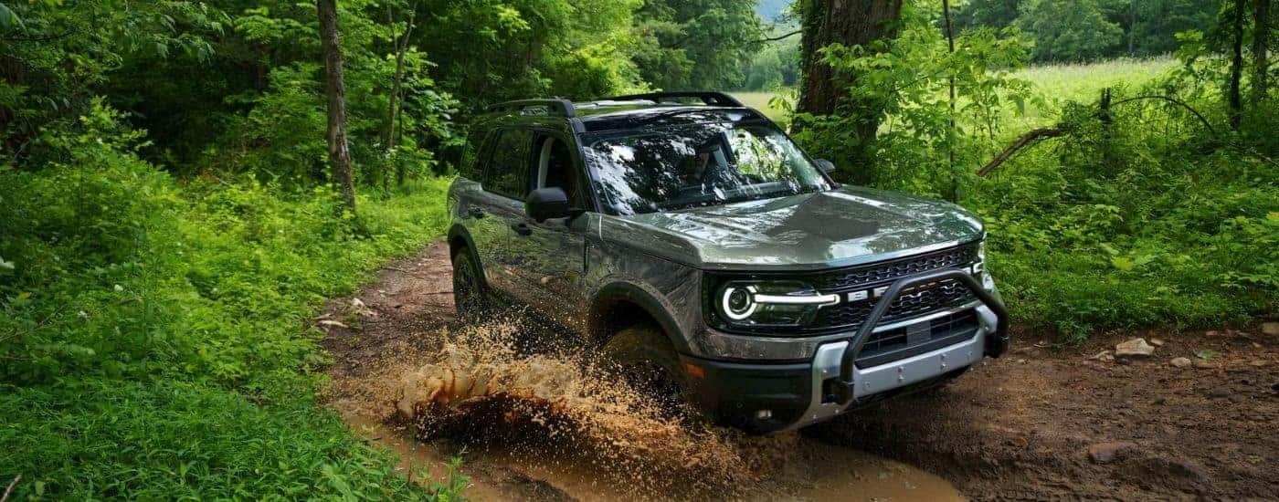 A gray 2026 Ford Bronco Sport shown driving a muddy trail in the woods.