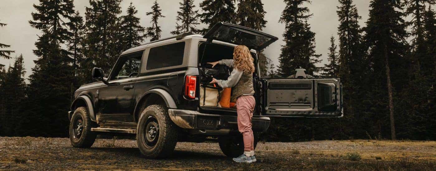 Black 2026 Ford Bronco parked in the forrest with a woman loading the cargo area.