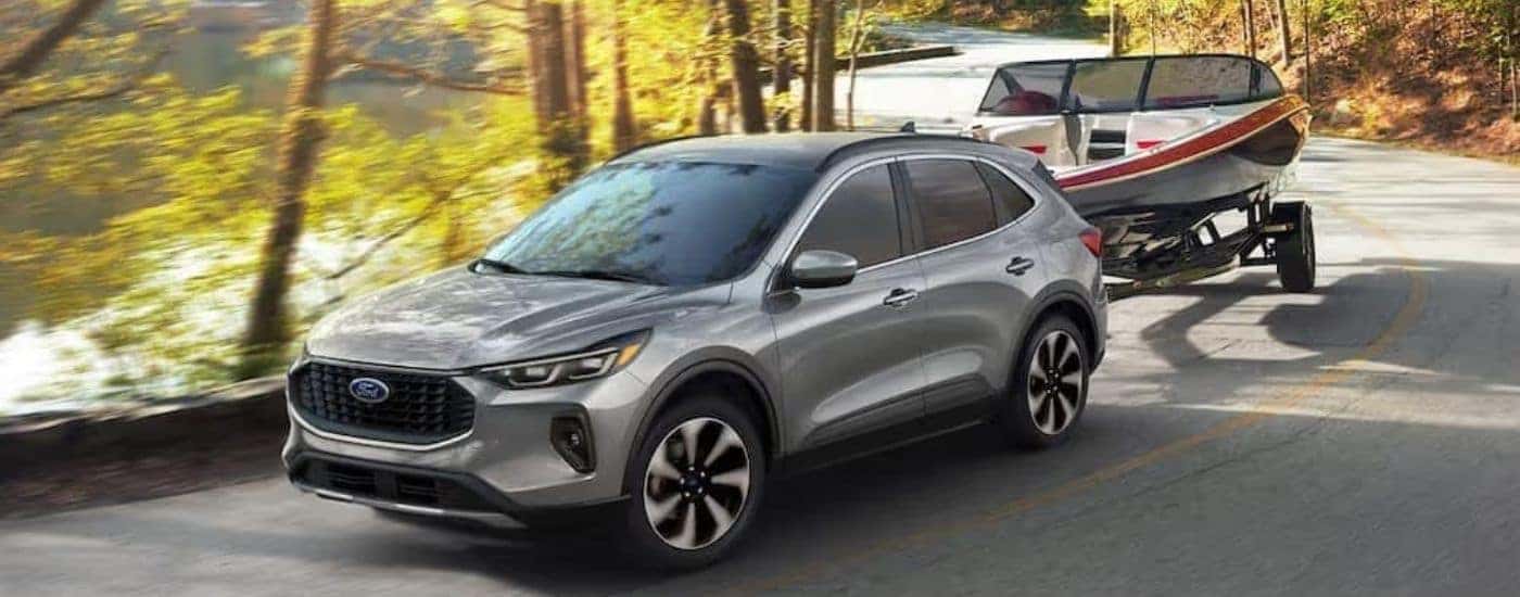 A silver 2024 Ford Escape is towing a boat on a windy road.