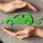 Two hands protecting a green eco-friendly car is shown.