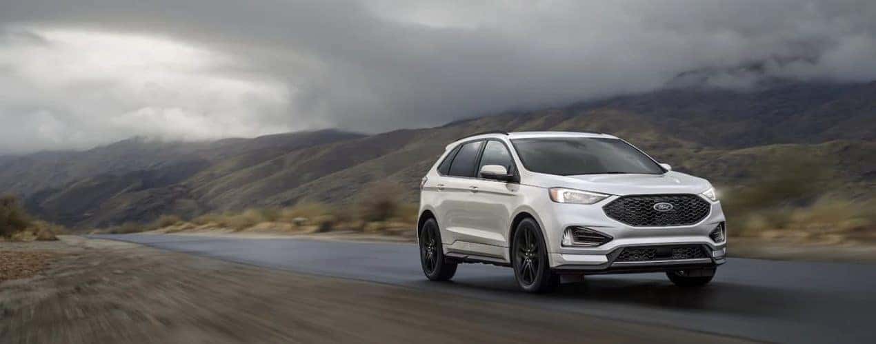 A silver 2022 Ford Edge ST-Line is shown driving down an empty road.