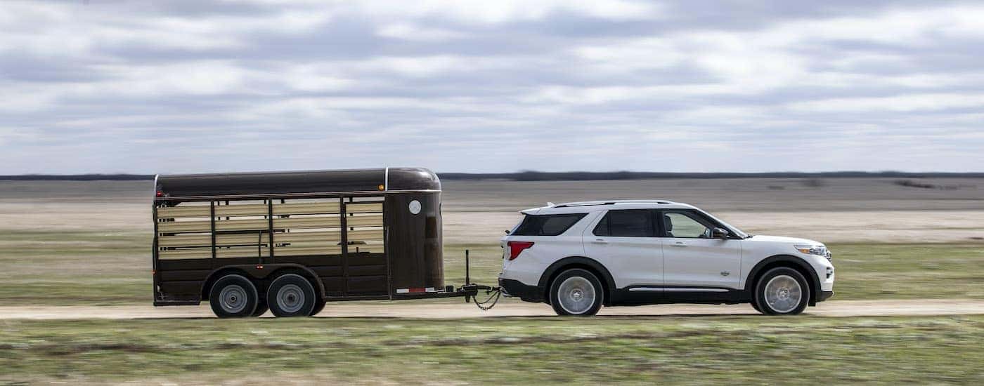 A white 2021 Ford Explorer King Ranch is shown from the side towing a trailer down an empty road.
