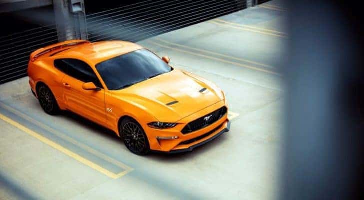 An orange 2018 Ford Mustang GT is shown parked on a parking garage.
