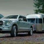A silver 2022 Ford F-150 is shown towing an Airstream trailer next to a lake.