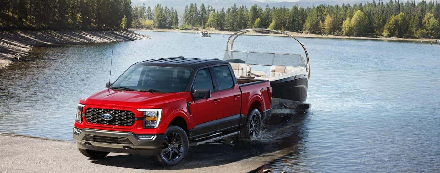 A red 2023 Ford F-150 Heritage is shown towing a boat out of a lake.