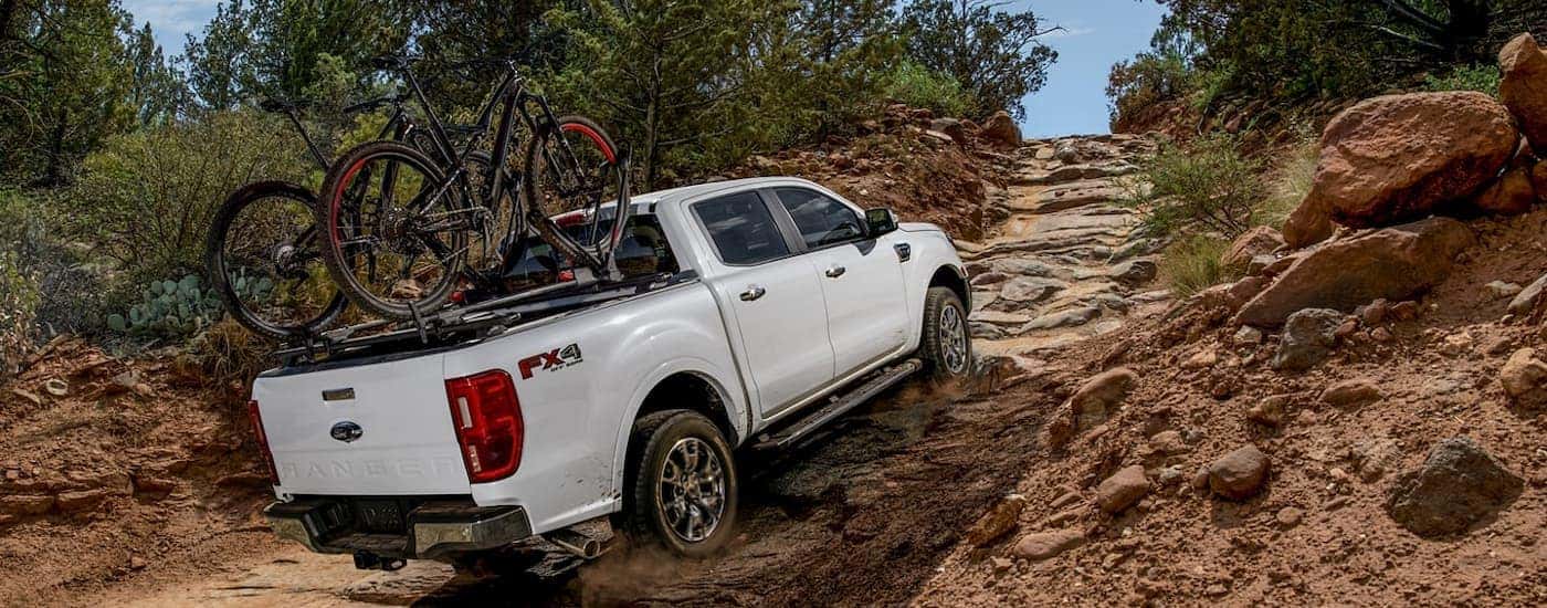 A white 2022 Ford Ranger Lariat is shown from the rear driving up a steep rocky trail.