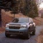 A blue 2022 Ford Maverick is shown driving on a dirt road.
