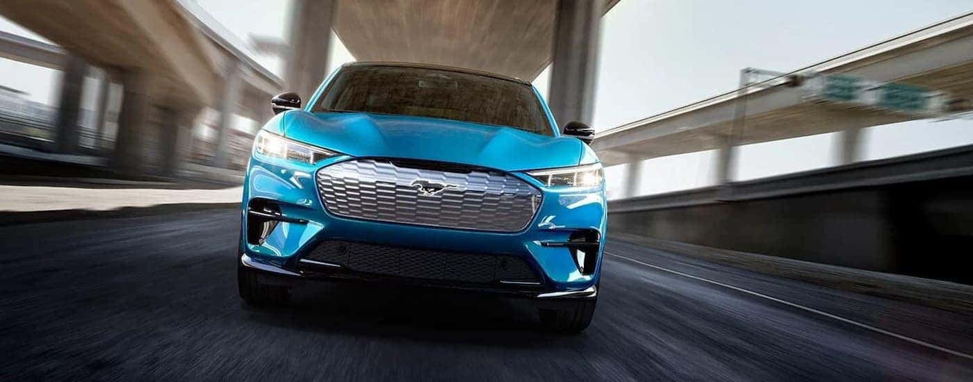 A blue 2022 Ford Mustang Mach-E is shown from the front driving on a highway.