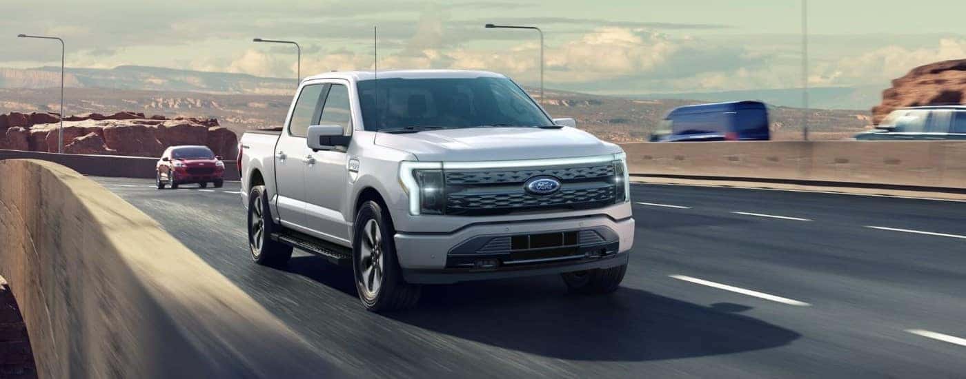 A white 2022 Ford F-150 Lightning is shown driving on an open highway.