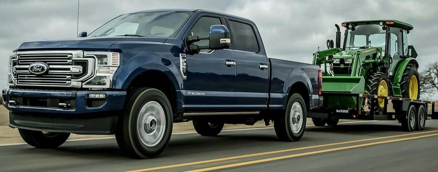 A blue 2022 Ford F-350 Limited towing a tractor.