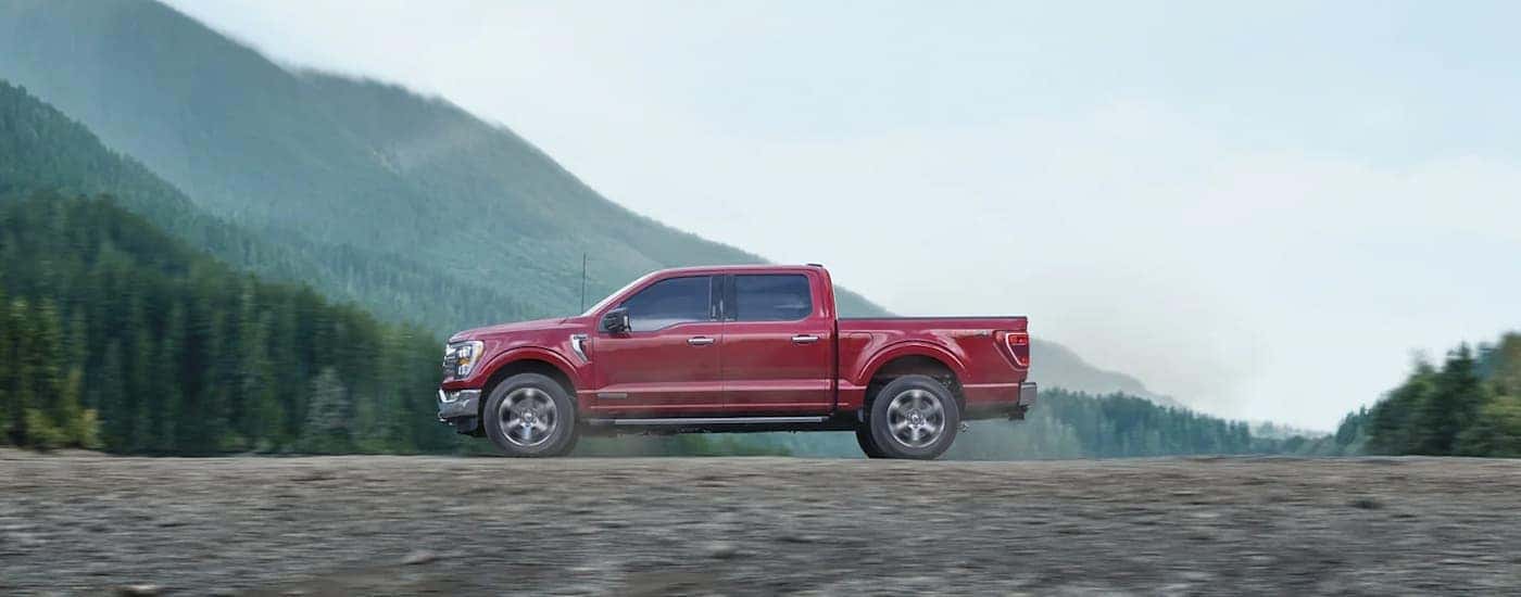 A red 2023 Ford F-150 is shown from the side driving on a dirt trail.