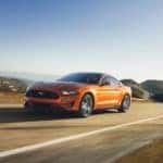 An orange 2018 Ford Mustang is shown driving on an open road after leaving a used Ford dealer.