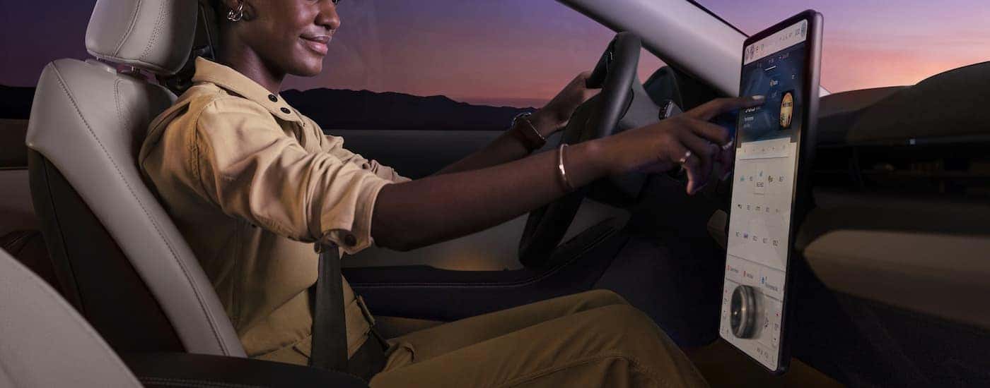A woman is shown using the infotainment screen while driving a 2023 Ford Mustang Mach-E.