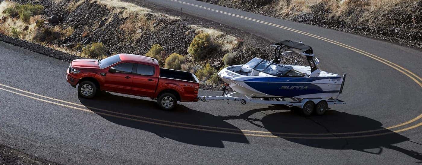 A red 2023 Ford Ranger XLT is shown towing a white and blue boat on a winding road.