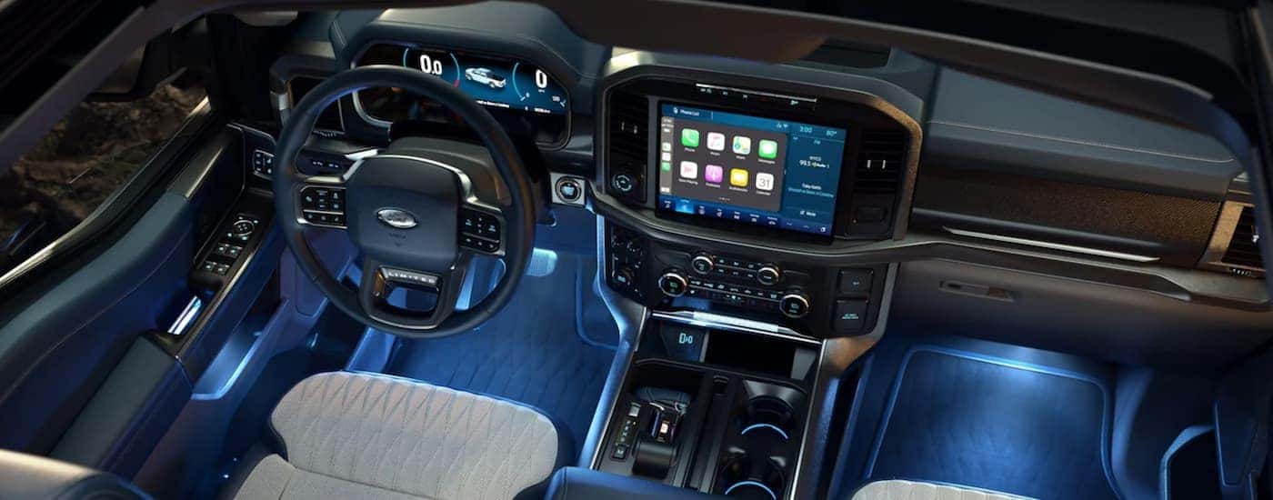 The front seats, dash, and blue footwell lighting is shown in a 2022 Ford F-150.
