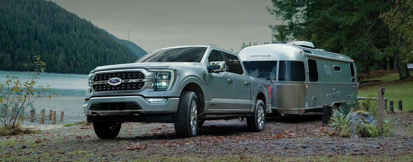 A silver 2022 Ford F-150 is shown towing an Airstream trailer near a lake.