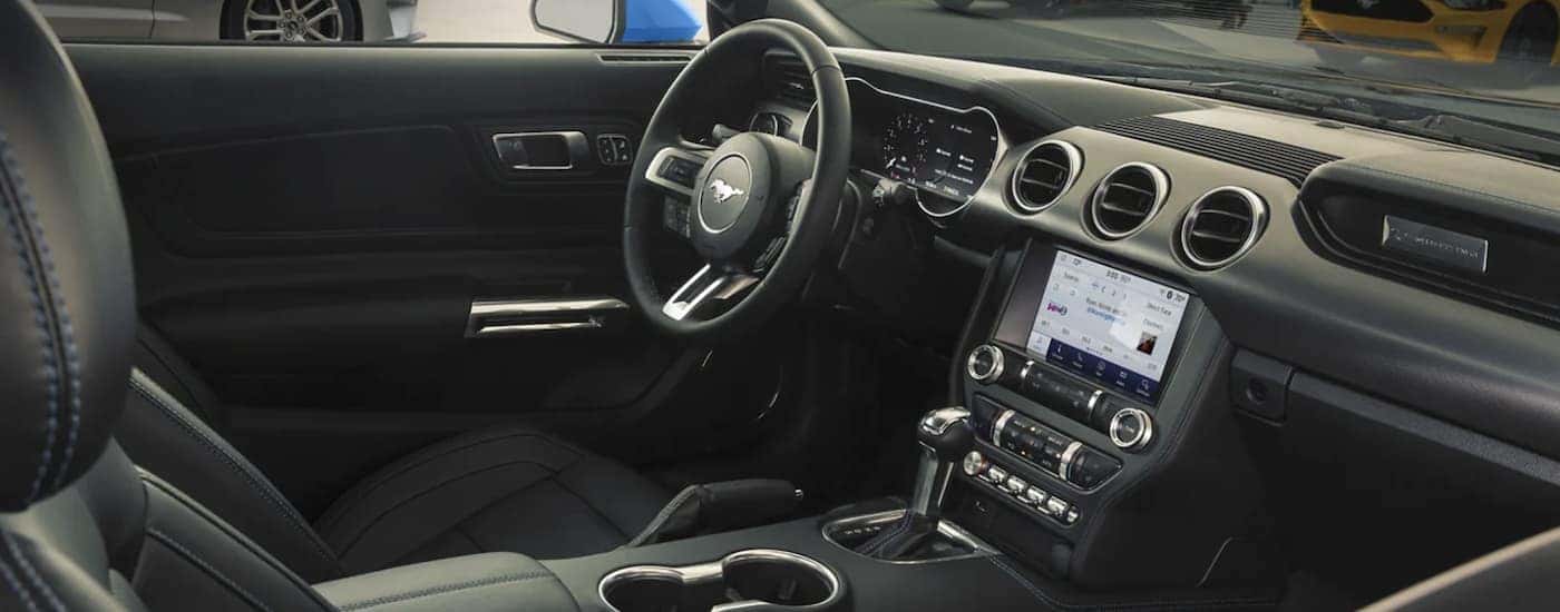The black interior of a 2022 Ford Mustang shows the steering wheel and infotainment screen.