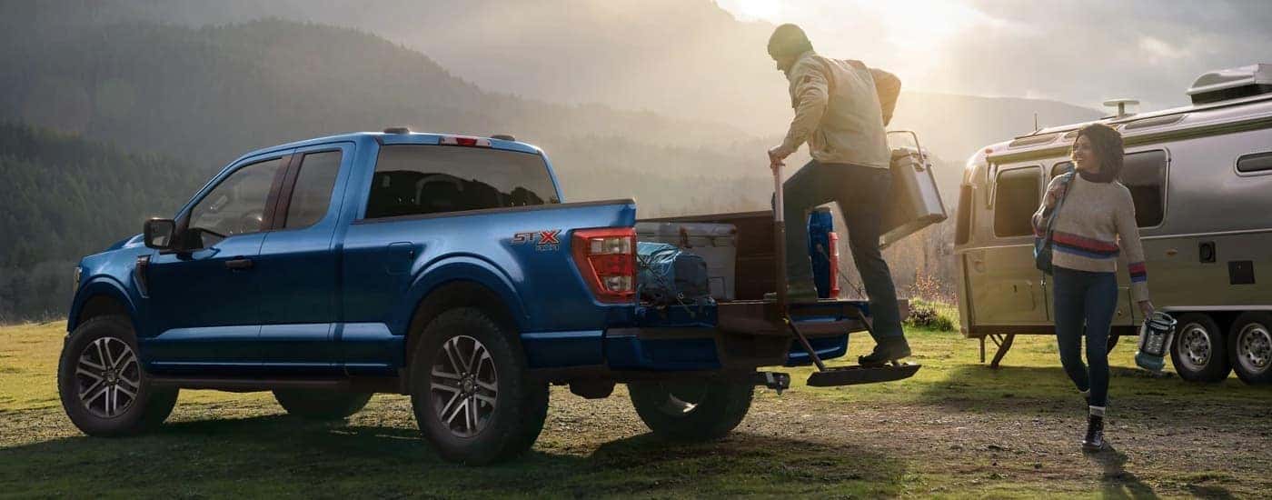 A man is shown getting gear from the bed of a blue 2023 Ford F-150 STX at a camping site.