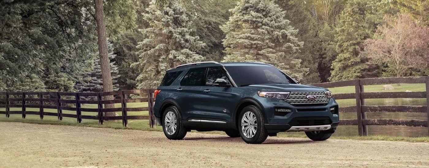 A blue 2023 Ford Explorer King Ranch is shown parked next to a fence on a farm.