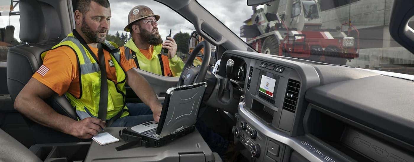 A construction worker is shown viewing a laptop in the cab of a 2023 Ford F-450.