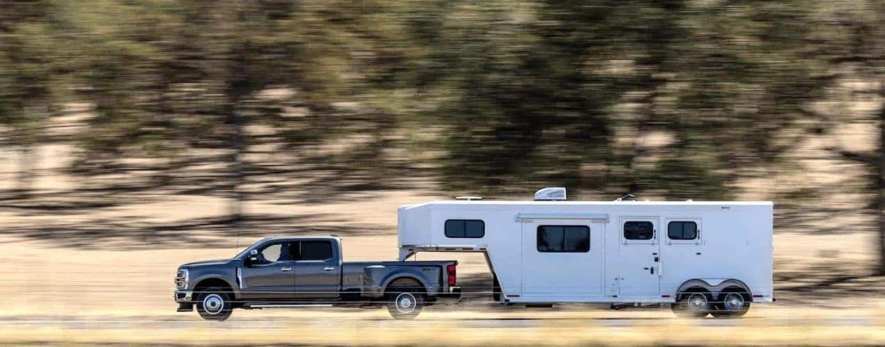 A grey 2023 Ford F-350 Super Duty Lariat is shown from the side towing a white trailer.