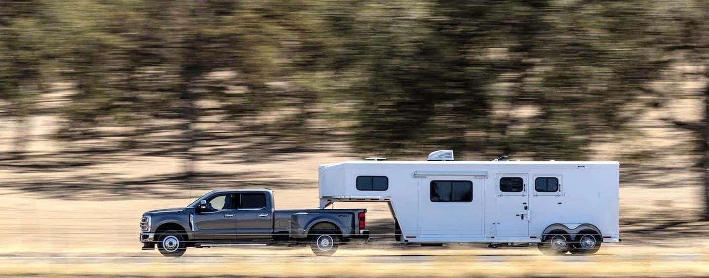 A grey 2023 Ford F-350 Super Duty Lariat is shown from the side towing a white trailer.