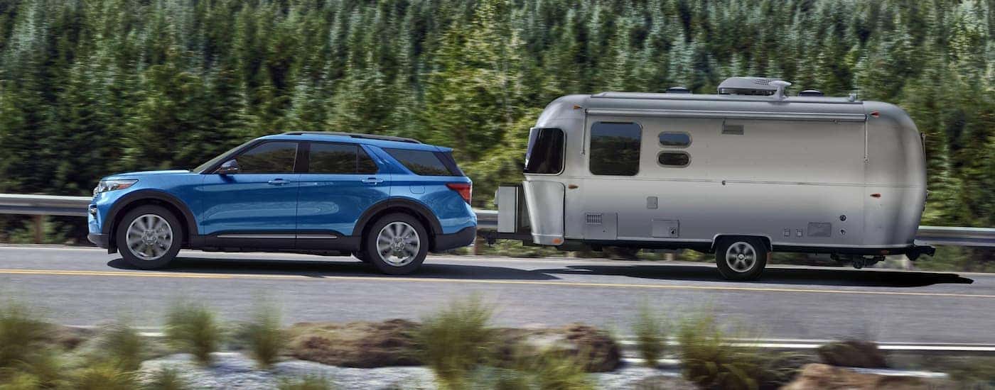 A blue 2021 Ford Explorer is shown towing an Airstream trailer on a tree-lined road.