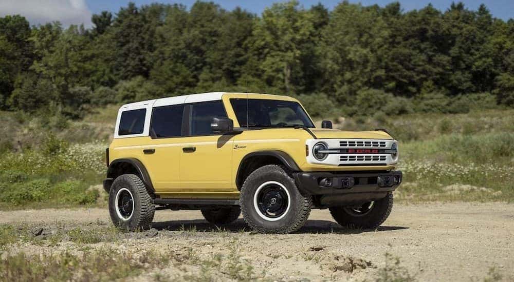 A yellow 2023 Ford Bronco Heritage Limited Edition is shown parked near a tree line.
