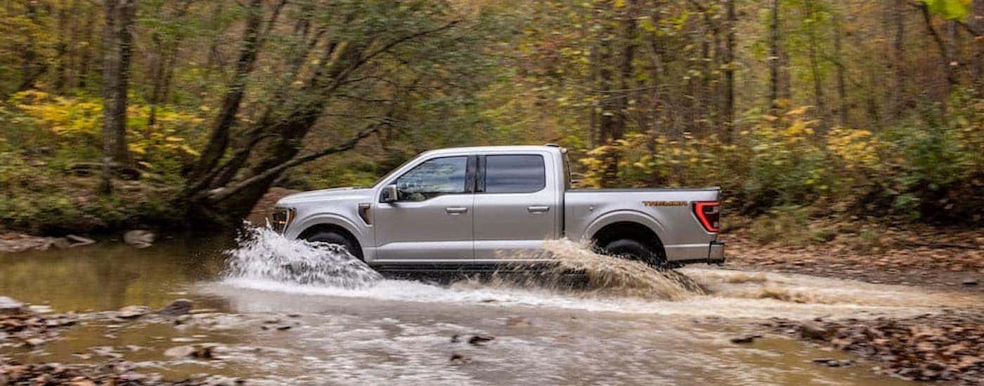 A silver 2021 Ford F-150 Tremor is shown from the side while driving through mud.