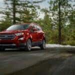 A red 2021 Ford EcoSport is shown driving past snowy trees.