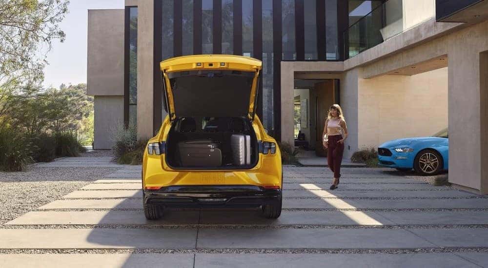 A yellow 2023 Ford Mustang Mach-E and blue Mustang are shown parked on the driveway of a modern house.