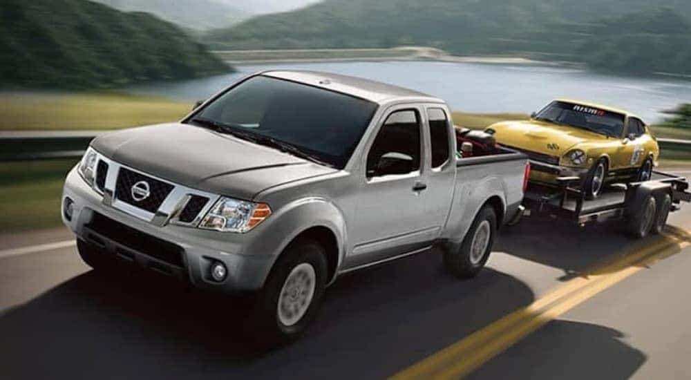 A silver 2020 Nissan Frontier is shown towing a car.