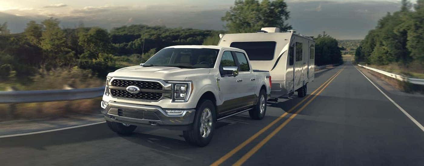 A white 2021 Ford F-150 is shown towing a trailer on a highway.
