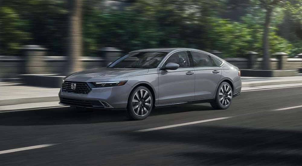 A grey 2023 Honda Accord Touring Hybrid is shown driving in a city.