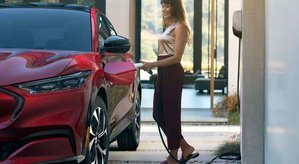 A person is shown charging a red 2024 Ford Mustang Mach-E for sale.